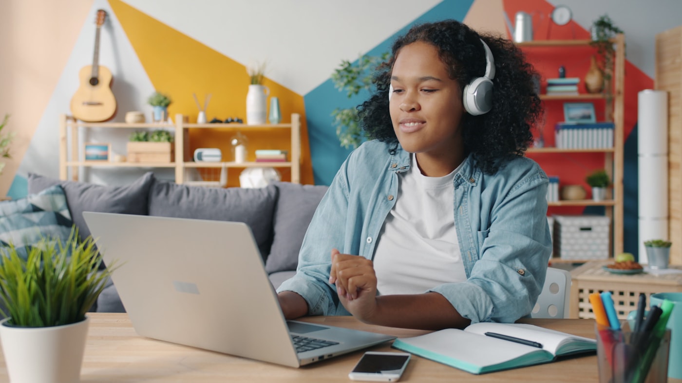Adolescente tomando una clase virtual desde casa, con audífonos y su cuaderno junto al computador